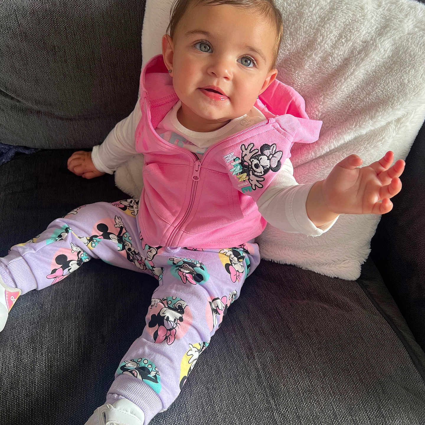 Amelia-Rose is registered to the contest to win money with this photo: baby, casual_wear, child, cozy, cute, fashion, gray_couch, happy, indoor, minnie_mouse, pink_hoodie, playful, portrait, purple_bow, reaching_hand, seated, smiling, sneakers, toddler, white_pillow