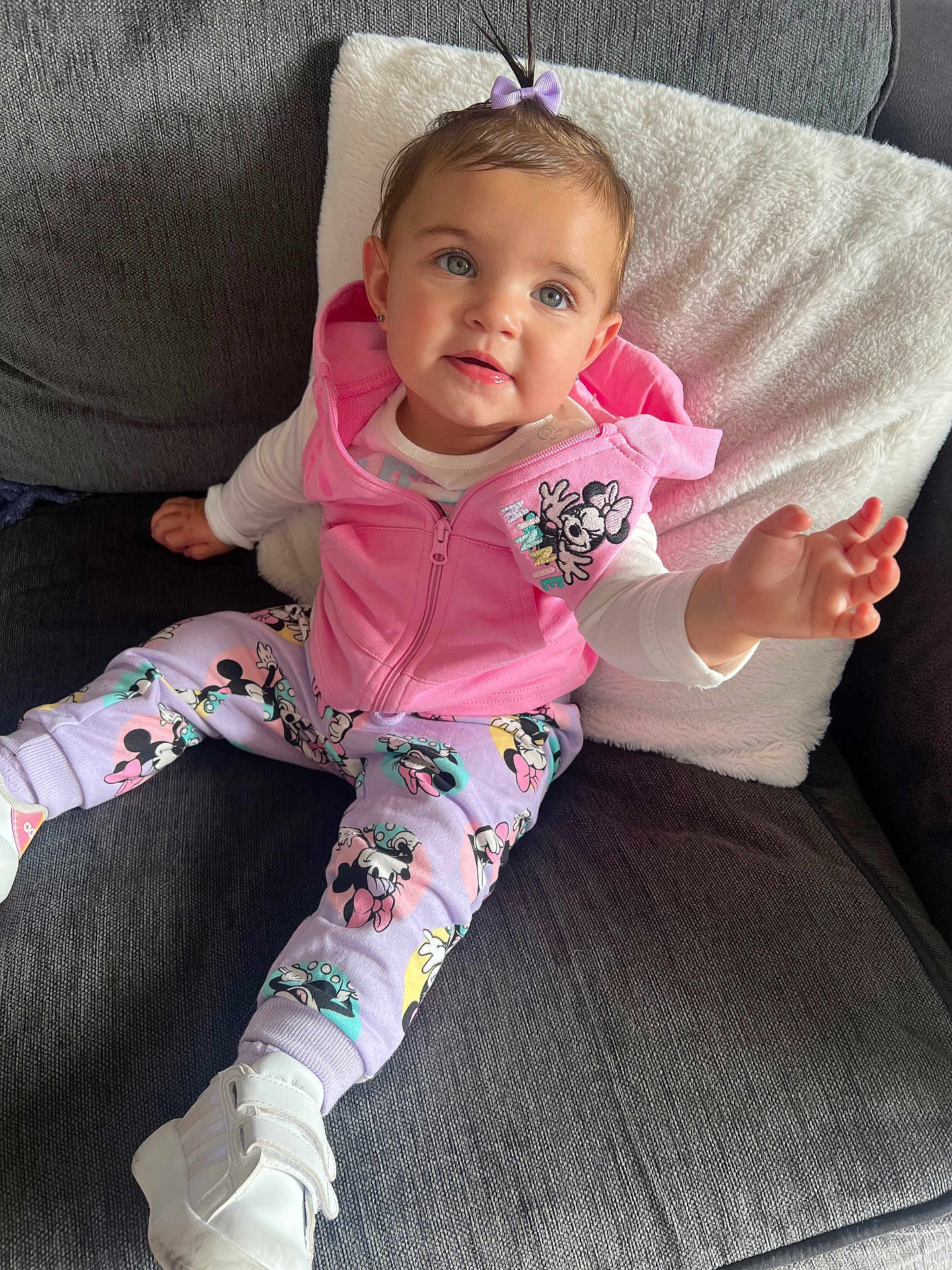 Amelia-Rose is registered to the contest to win money with this photo: toddler, child, pink_hoodie, minnie_mouse, purple_bow, white_pillow, gray_couch, sneakers, reaching_hand, cute, indoor, smiling, fashion, casual_wear, happy, portrait, seated, cozy, playful, baby