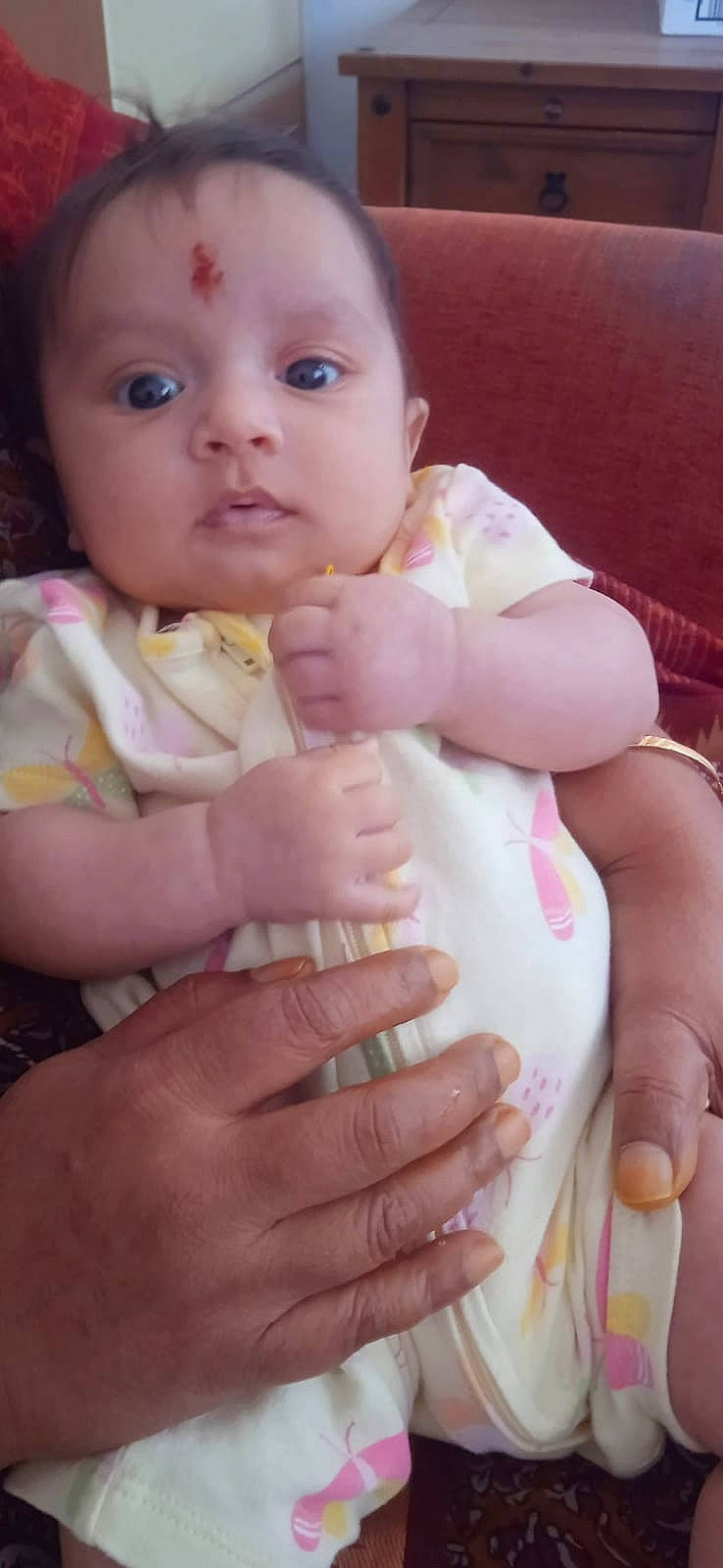 adult_hand, baby, butterfly_pattern, casual, child, closeup, clothing, comfort, couch, expression, face, furniture, hand, holding, indoor, infant, person, sitting, skin, wooden_cabinet