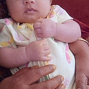 Maghathi joined the competition — help win amazing prizes! baby, infant, child, hand, adult_hand, couch, clothing, butterfly_pattern, face, person, indoor, furniture, wooden_cabinet, sitting, closeup, skin, expression, comfort, holding, casual