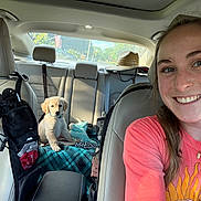 Leonie is registered to the contest to win money with this photo: woman, smile, selfie, car_interior, puppy, golden_retriever, blanket, seat, headrest, hat, sunlight, collar, travel, young_adult, happy, casual_clothing, window, daytime, leather_seat, accessory