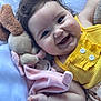 baby, child, smile, happy, plush_toy, blanket, yellow_clothing, curly_hair, cute, infant, closeup, face, hand, lying_down, soft_toy, comfort, indoors, skin, expression, adorable