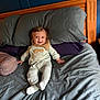 baby, bed, pajamas, smile, happy, child, pillow, blanket, wood, headboard, indoors, person, sleepwear, comfort, rest, furniture, cute, infant, cozy, relaxation