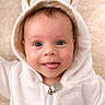 baby, child, hoodie, bunny_ears, tongue_out, cute, infant, smiling, face, portrait, soft_background, white_clothing, playful, close_up, young_child, warm_tone, happy, expression, indoor, adorable