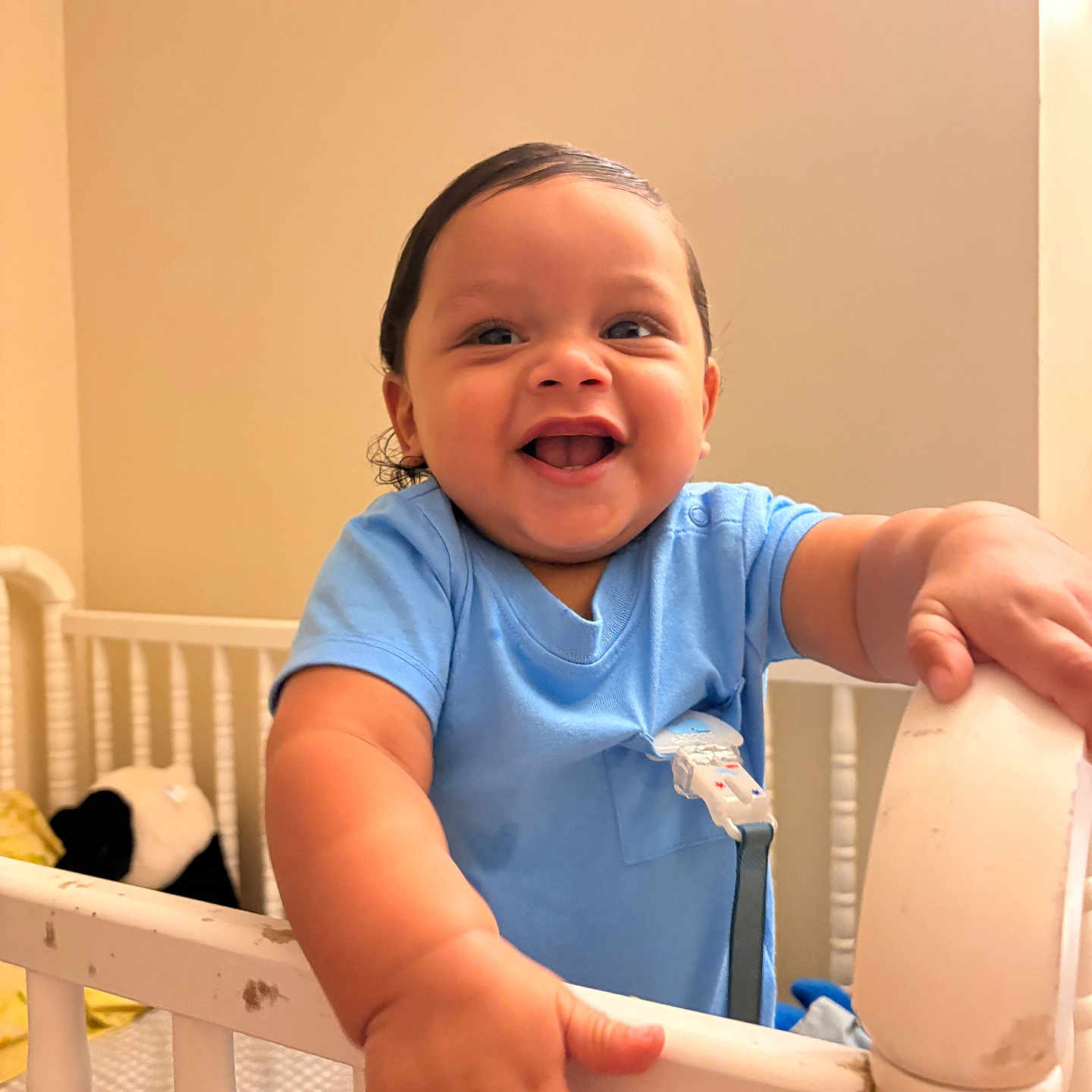 Felix is registered to the contest to win money with this photo: baby, blue_clothing, crib, smiling, happy, infant, child, indoor, nursery, furniture, hand, face, person, cute, young_child, warm_lighting, home, portrait, baby_girl, baby_boy
