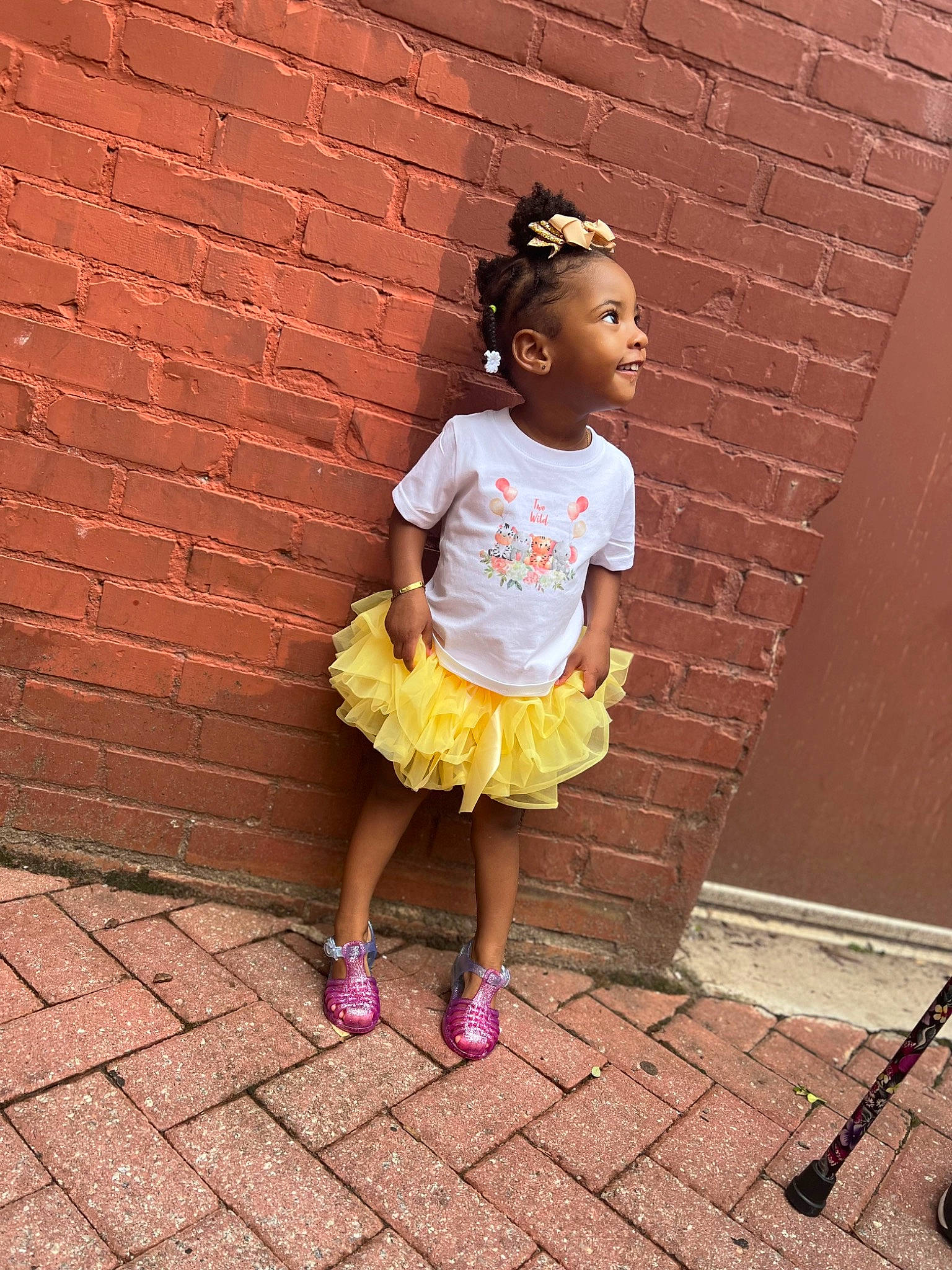 Denver is registered to the contest to win money with this photo: brick, brickwork, child, eyewear, facial_expression, flooring, fun, happy, human_leg, leisure, magenta, person, pink, sandal, sidewalk, sitting, summer, t_shirt, tints_and_shades, toddler