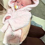 Phoebe is registered to the contest to win money with this photo: baby, carpet, child, clothing, cozy, cushion, cute, hand, hooded_clothing, human, indoor, infant, newborn, pacifier, person, pink_robe, resting, sleepy, soft_texture, warm