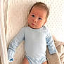 baby, infant, onesie, blue_clothing, blanket, soft_texture, face, skin, cute, newborn, lying_down, indoors, portrait, baby_bed, curious, head, eyes, small_hands, cozy, resting