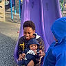 children, baby, toddler, siblings, playground, slide, purple_slide, outdoor, smiling, sitting, holding_baby, infant, winter_clothing, hooded_jacket, blue_coat, playground_equipment, rubber_floor, family, daylight, portrait