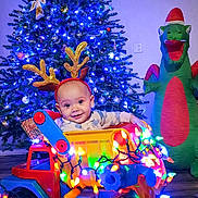 Jaxon is registered to the contest to win money with this photo: baby, reindeer_ears, toy_truck, christmas_lights, christmas_tree, inflatable_dragon, holiday, festive, smiling, indoor, flooring, decorations, colorful, child, playful, seasonal, bright, cute, happy, celebration
