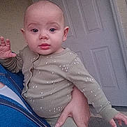 Jaxon is registered to the contest to win money with this photo: baby, child, person, infant, onesie, green_clothing, hand, face, door, indoor, adult_hand, blue_jacket, curious, expression, portrait, holding, young_child, skin, head, long_sleeve