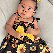 Evangelinne is registered to the contest to win money with this photo: baby, child, girl, dress, sunflower, yellow_bow, headband, couch, soft_fabric, footwear, black_slippers, indoors, cute, portrait, infant, clothing, fashion, smiling, baby_hands, cozy