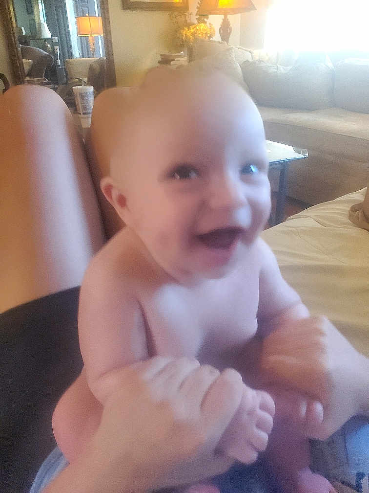 Zane joined the competition — help win amazing prizes! baby, smiling, hands, legs, adult_hands, living_room, sofa, lamp, table, couch, happy, indoor, person, blur, skin, playful, furniture, child, home, infant
