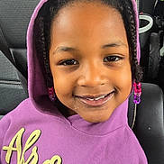 Zariyah is registered to the contest to win money with this photo: child, smiling, hoodie, purple_clothing, braids, beads, car_seat, seatbelt, portrait, indoors, happy, person, cute, young_child, casual, fashion, headwear, face, sitting, closeup