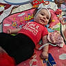 baby, play_mat, toy, headband, red_shirt, smiling, lying_down, colorful, princess, prince, blanket, indoor, child, infant, cute, person, soft_toy, clothing, happy, decorative