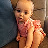 baby, child, bow, red_bow, pink_clothing, couch, blue_pillow, indoors, infant, cute, sitting, foot, hand, face, eyes, skin, furniture, expression, young_child, portrait