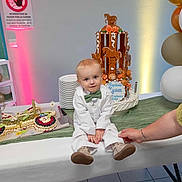 Lyam a rejoint le concours — aidez-le/la à gagner de superbes lots ! toddler, child, white_suit, green_bow_tie, birthday_cake, horse_cake, dessert, train_cake, table, hand, balloons, party, celebration, indoor, floor_tiles, plated_dishes, knife, flower_decor, light, person