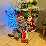 Lyam a rejoint le concours — aidez-le/la à gagner de superbes lots ! toddler, child, santa_hat, christmas_tree, ornaments, holiday, gift_box, floor_tiles, olaf_figure, santa_decoration, indoor, festive, lights, decorations, seated, curious, holiday_spirit, winter, celebration, home
