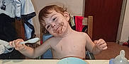 Andrès participe au concours pour gagner de l'argent avec cette photo : child, toddler, messy_face, chocolate, bowl, spoon, high_chair, table, food, water_bottle, plate, indoor, smiling, happy, messy, clothing, face, person, dining, home