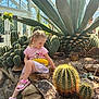 Liza joined the competition — help win amazing prizes! child, girl, cactus, greenhouse, plants, rocks, sunlight, pink_clothing, sandals, agave, nature, indoor, curious, spiky, desert_plants, potted_plants, person, casual_wear, daylight, exploration