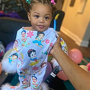Sarah joined the competition — help win amazing prizes! toddler, child, pajamas, hair_clips, hand, balloons, living_room, carpet, furniture, cartoon_characters, smile, cute, indoor, person, clothing, pattern, young_child, bright_colors, soft_furniture, home