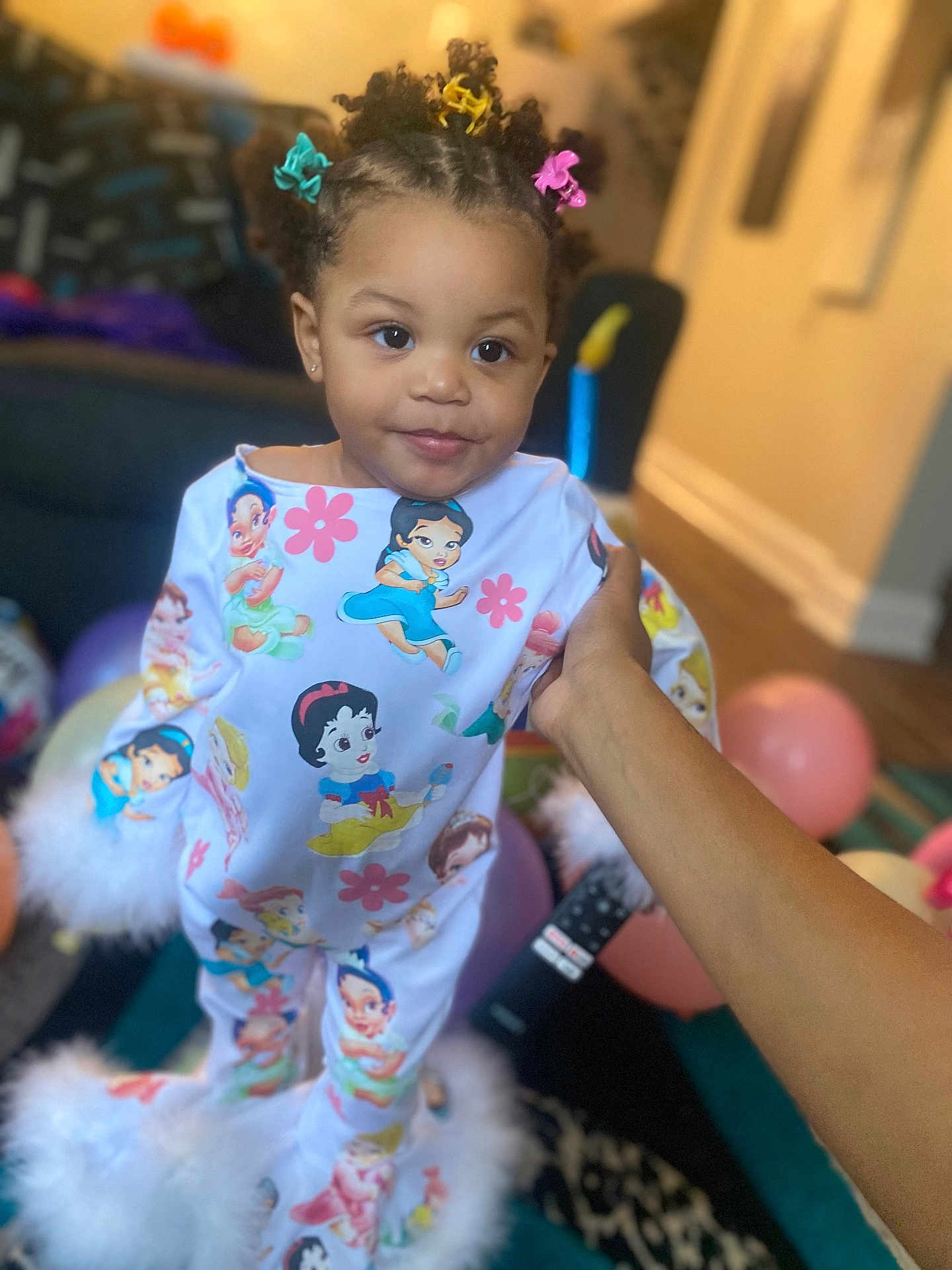Sarah joined the competition — help win amazing prizes! toddler, child, pajamas, hair_clips, hand, balloons, living_room, carpet, furniture, cartoon_characters, smile, cute, indoor, person, clothing, pattern, young_child, bright_colors, soft_furniture, home