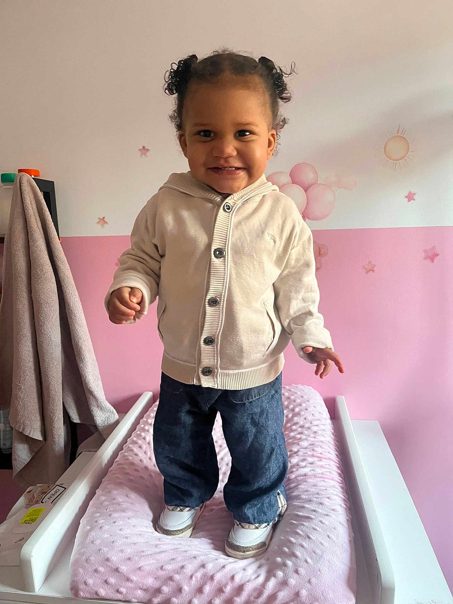 Mahyna a rejoint le concours — aidez-le/la à gagner de superbes lots ! child, toddler, smile, standing, nursery, changing_table, pink, hoodie, jeans, sneakers, pigtails, hair_buns, wall_stickers, stars, balloons, sun, towel, indoor, happy, portrait