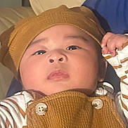 Dream Johnson Iv joined the competition — help win amazing prizes! baby, child, infant, brown_hat, brown_outfit, striped_shirt, face, person, hand, couch, indoor, portrait, holding, young_child, cozy_clothing, cute, looking_up, skin_tone, buttoned_overall, mobile_screenshot