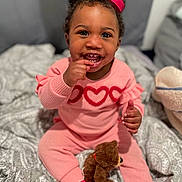 Damari joined the competition — help win amazing prizes! baby, bed, blanket, bow, child, cozy, curly_hair, cute, face, happy, hearts, indoors, patterned_blanket, person, pink_outfit, sitting, smiling, teddy_bear, toddler, toy