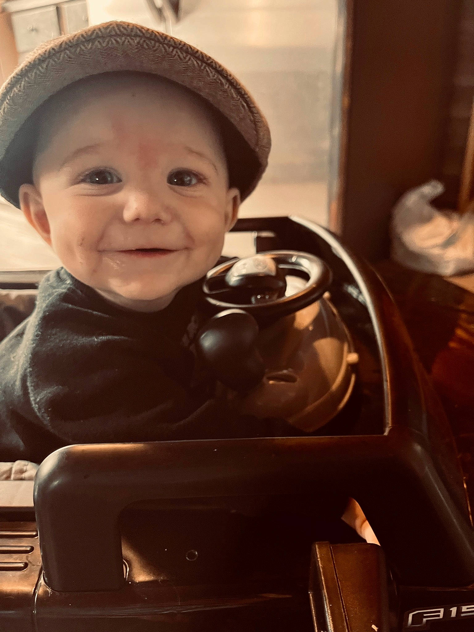 Coleson is registered to the contest to win money with this photo: auto_part, automotive_design, automotive_exterior, automotive_wheel_system, baby, black_hair, cap, child, fashion_accessory, flash_photography, fun, happy, hat, headwear, joy, motor_vehicle, person, sitting, smile, steering_wheel