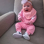 Harper joined the competition — help win amazing prizes! baby, child, pink_clothing, headband, flower, bib, sneakers, armchair, gray_furniture, smiling, happy, sitting, indoor, cute, young_child, portrait, small_hands, footwear, fabric, cozy