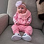 Harper is registered to the contest to win money with this photo: baby, pink_tracksuit, bib, headband, flower, white_shoes, sitting, armchair, gray_fabric, happy, child, indoor, portrait, cute, smiling, infant, clothing, footwear, baby_girl, comfortable