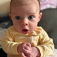 Violet joined the competition — help win amazing prizes! baby, infant, face, hands, yellow_clothing, onesie, expression, surprised, wide_eyes, indoor, closeup, portrait, child, cute, soft_light, floral_pattern, table, skin, person, newborn