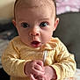 baby, infant, face, hands, yellow_clothing, onesie, expression, surprised, wide_eyes, indoor, closeup, portrait, child, cute, soft_light, floral_pattern, table, skin, person, newborn