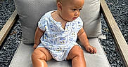 Noah is registered to the contest to win money with this photo: baby, child, outdoor, chair, cushion, romper, sandals, curly_hair, skin, person, seated, fence, gravel, wood, footwear, expression, summer, casual, cute, infant