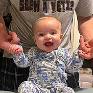 Mallory joined the competition — help win amazing prizes! baby, child, infant, smiling, happy, blue_flower_onesie, holding_hands, adult, gray_tshirt, text_on_shirt, indoor, person, portrait, cute, joyful, seated, hands, face, expression, clothing