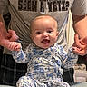 baby, child, infant, smiling, happy, blue_flower_onesie, holding_hands, adult, gray_tshirt, text_on_shirt, indoor, person, portrait, cute, joyful, seated, hands, face, expression, clothing