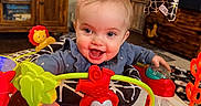 Mallory joined the competition — help win amazing prizes! baby, child, smiling, toy, activity_center, indoor, furniture, wooden_cabinet, television, colorful, play, happy, clothing, hand, face, head, room, living_room, elephant_toy, lion_toy