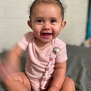 Miracle joined the competition — help win amazing prizes! baby, child, smiling, pink_clothing, sitting, indoor, cute, happy, face, infant, person, skin, hand, foot, pacifier_clip, short_hair, playful, blur, light, background