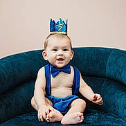 Beau is registered to the contest to win money with this photo: baby, blue, bow_tie, celebration, chair, child, clothing, crown, cute, happy, headwear, indoor, infant, person, plush, portrait, sitting, smile, suspenders, young
