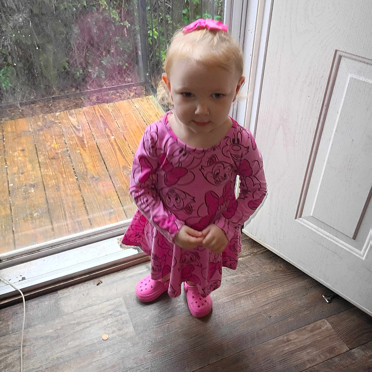 Madison is registered to the contest to win money with this photo: child, girl, indoor, pink_dress, pink_shoes, window, glass_door, wooden_floor, wooden_deck, greenery, standing, looking_up, shy_expression, hair_bow, floor, door, clothing, person, young, casual