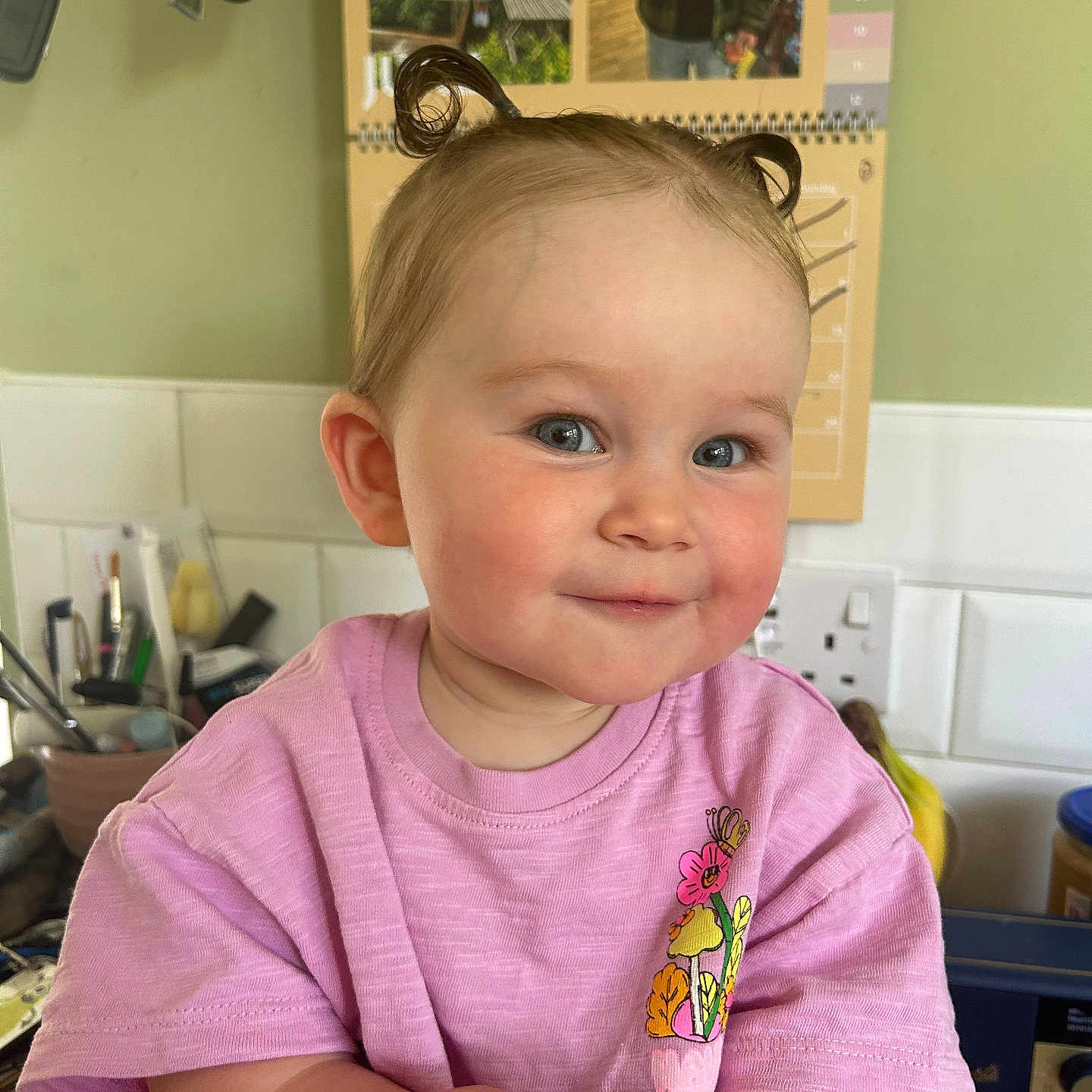 Anna is registered to the contest to win money with this photo: casual, child, counter, cupboard, curly_hair, cute, face, food, happy, holding, home, indoor, kitchen, pastry, person, pink_shirt, portrait, smiling, toddler, young_child