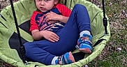 Carsen is registered to the contest to win money with this photo: child, toddler, swing, playground, outdoor, grass, leaves, portrait, sitting, serious, curly_hair, face, eyes, shirt, pants, sneakers, green_swing, backyard, daylight, recreation
