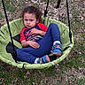 child, toddler, swing, playground, outdoor, grass, leaves, portrait, sitting, serious, curly_hair, face, eyes, shirt, pants, sneakers, green_swing, backyard, daylight, recreation