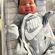 Wysdom is registered to the contest to win money with this photo: baby, newborn, infant, onesie, nike, pacifier, blanket, hospital, sleeping, smiling, cute, face, clothing, bed, comfort, closeup, person, softlighting, indoor, resting