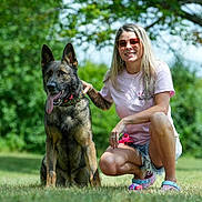 Ares The Malinois is registered to the contest to win money with this photo: dog, woman, person, outdoor, grass, park, trees, nature, portrait, sitting, smiling, sunglasses, blonde_hair, tattoos, collar, leash, german_shepherd, animal, daylight, pet
