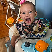 Avaya is registered to the contest to win money with this photo: baby, child, walker, toy, smiling, happy, indoor, person, headband, flower, clothing, hand, blue, orange, furniture, floor, wood, bandana, cheerful, portrait