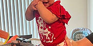 Avaya is registered to the contest to win money with this photo: adult, bow, candle, celebration, child, hand, happy, high_chair, indoor, kitchen, leopard_print, person, plastic_cup, red_shirt, shorts, smiling, spoon, table, toddler, window_blinds