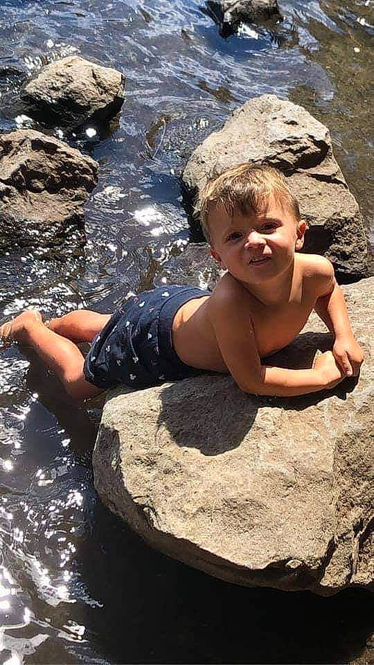 Timéo participe au concours pour gagner de l'argent avec cette photo : arm, barechested, beach, bedrock, body_of_water, chest, eye, fun, geology, hand, human_body, leisure, people_in_nature, person, recreation, rock, sitting, smile, thigh, toddler