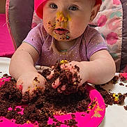 Mia is registered to the contest to win money with this photo: baby, child, high_chair, cake, chocolate, messy, pink_hat, pink_plate, birthday, celebration, balloon, face_paint, food, smiling, indoor, table, person, cute, toddler, fun